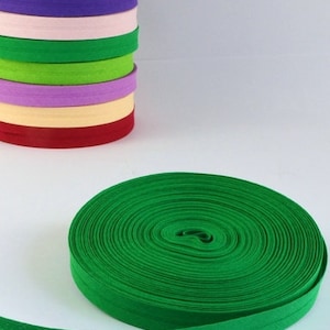 Puede incluir: Primer plano de un rollo de ribete elástico verde brillante. El ribete está doblado y enrollado, mostrando las múltiples capas de la tela.