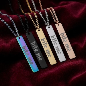May include: Five vertical bar pendant necklaces on thin metal chains. Each pendant features the engraved text 'bite me'. The pendants are finished in iridescent rainbow, matte black, gold, silver, and rose gold tones, each hanging from a matching chain.