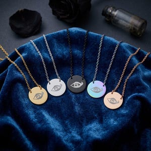May include: A collection of six circular pendant necklaces, each featuring an engraved eye symbol. The set includes gold, silver, black, iridescent, and rose gold finishes, all suspended on matching metal link chains of varying lengths.