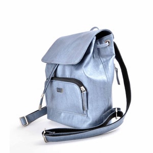 May include: A light blue backpack made of cork with a drawstring closure and a zipped pocket. The backpack has adjustable straps and a silver logo.