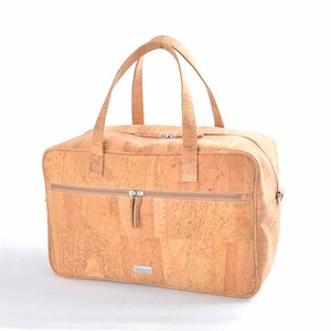 Könnte beinhalten: Eine hellbraune Kork-Reisetasche mit zwei oberen Griffen und einem Reißverschluss. Die Tasche hat eine kleine Reißverschlusstasche vorne und ein Markenetikett mit der Aufschrift "Corkor."
