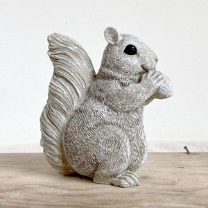 May include: A grey squirrel figurine holding a nut in its paws. The squirrel has a bushy tail and a detailed, realistic design.