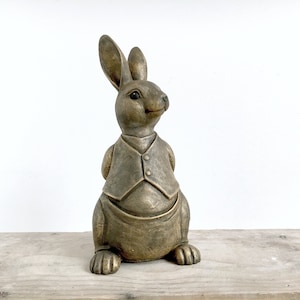 Könnte beinhalten: Eine goldfarbene Hasenfigur mit Weste in stehender Pose. Der Hase hat ein detailliertes Gesicht und ist aus einem strukturierten Material gefertigt.