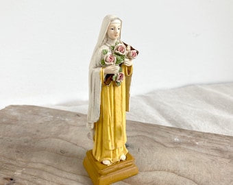 May include: A white and yellow figurine of a woman holding a bouquet of pink roses. The figurine is standing on a gold base.