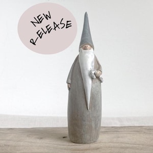 Op de afbeelding: Een grijze en witte gnoomfiguur met een blauwe hoed en een witte baard. De gnoom houdt een klein wit vogeltje in zijn rechterhand. De figuur staat op een houten oppervlak.