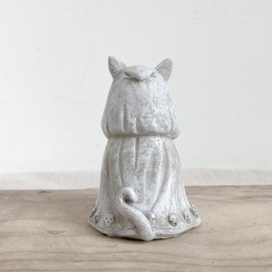 Puede incluir: Estatua de gato gris con un dise&ntilde;o de t&uacute;nica drapeada. El gato tiene orejas puntiagudas y una cola rizada. La base de la estatua est&aacute; adornada con peque&ntilde;os detalles de calaveras. La estatua est&aacute; hecha de un material texturizado.