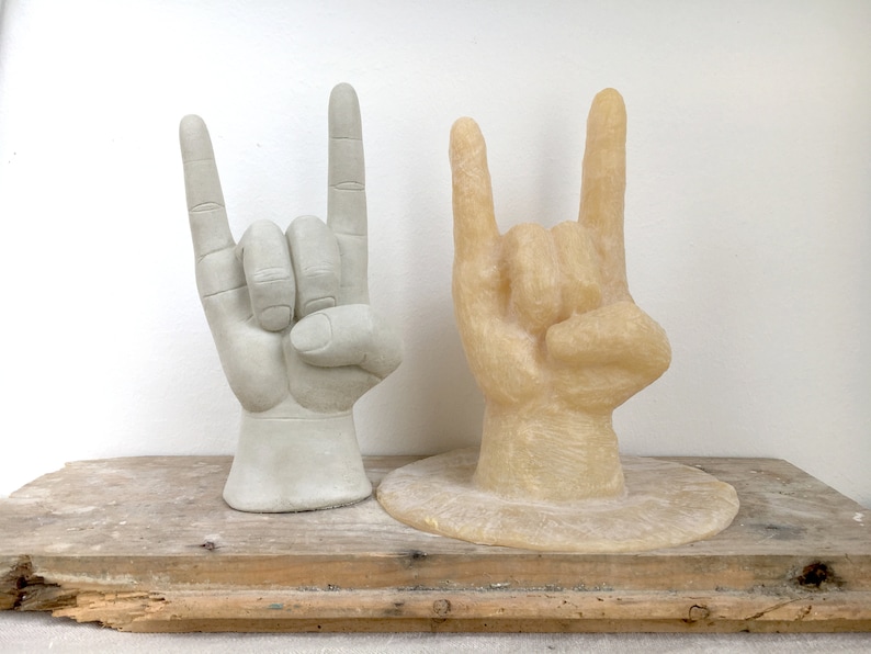 K&ouml;nnte beinhalten: Zwei Handskulpturen im 'Rock on'-Zeichen. Eine ist hellgrau, die andere hellbraun. Beide stehen auf einer verwitterten Holzoberfl&auml;che vor einem wei&szlig;en Hintergrund. Die Skulpturen sind wahrscheinlich Dekorationsartikel.