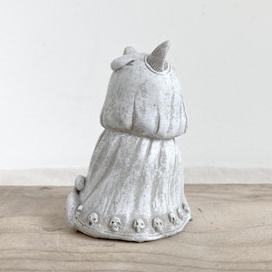 Puede incluir: Una figura gris con forma de gato con un acabado texturizado. El gato tiene orejas puntiagudas y una prenda drapeada. La base de la figura est&aacute; adornada con peque&ntilde;os detalles de calaveras, creando una est&eacute;tica g&oacute;tica &uacute;nica. La figura est&aacute; sobre una superficie de madera.