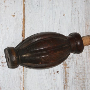Könnte beinhalten: Ein dunkelbraunes Holz-Finial mit geriffeltem Design und einem runden Knopf an einem Ende. Das Finial hat an dem anderen Ende einen hellbraunen Holzstift.