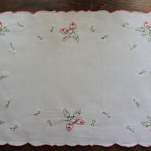 May include: White linen tea towel with red and green embroidered strawberries. The towel has a scalloped edge and the text "Diane Horbaly" is embroidered in the bottom left corner.