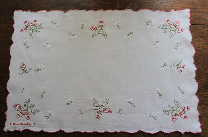 May include: White linen tea towel with red and green embroidered strawberries. The towel has a scalloped edge and the text "Diane Horbaly" is embroidered in the bottom left corner.