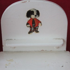 May include: White wooden chair with a black and white dog wearing a red and white checked shirt. The chair has a small shelf.