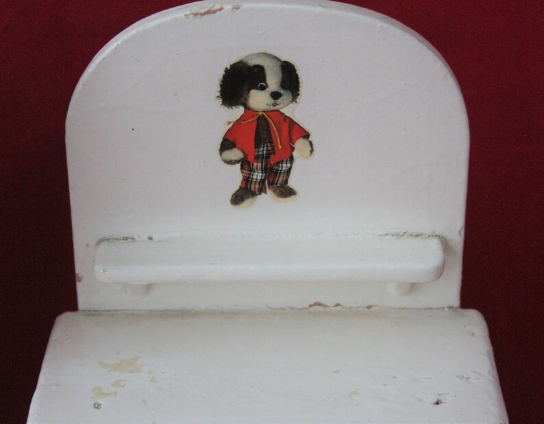 May include: White wooden chair with a black and white dog wearing a red and white checked shirt. The chair has a small shelf.