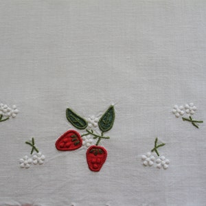 May include: White linen tea towel with embroidered red strawberries and white flowers.