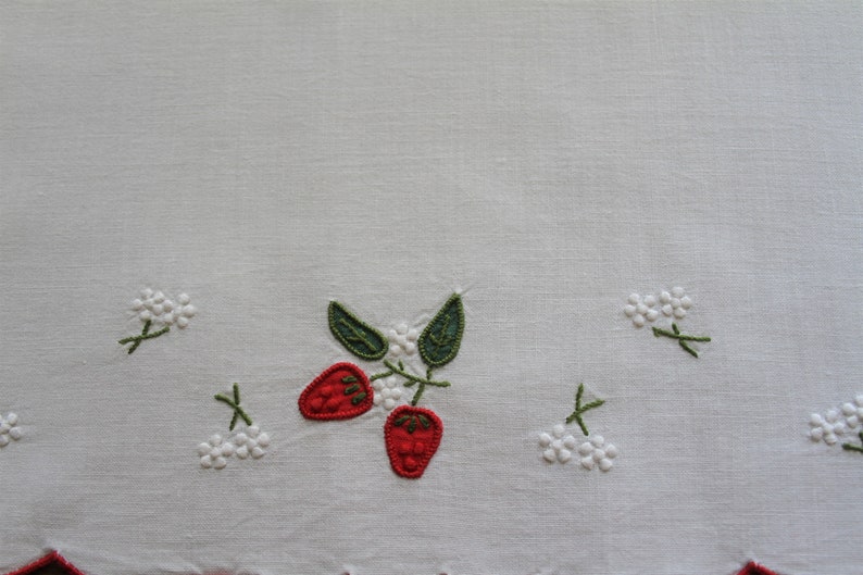 May include: White linen tea towel with embroidered red strawberries and white flowers.
