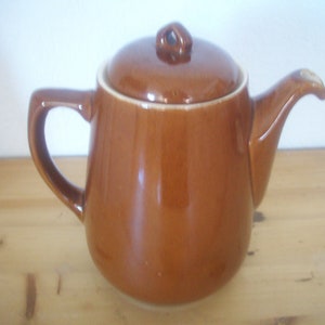 Könnte beinhalten: Eine braune Teekanne aus Keramik mit Deckel. Die Teekanne hat einen runden Körper und einen Griff an der Seite.