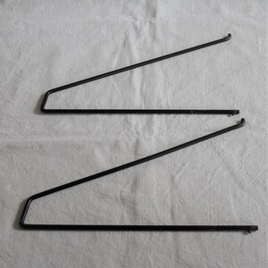 Könnte beinhalten: Zwei schwarze Metall-Regalhalterungen. Jede Halterung hat eine horizontale Basis, eine rechtwinklige Ecke und einen diagonalen Stützarm. Die Halterungen sind für die Aufnahme eines Regals konzipiert und werden auf weißem Hintergrund gezeigt.
