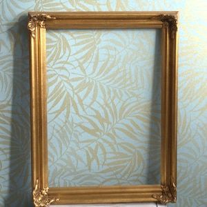 Könnte beinhalten: Ein rechteckiger, goldfarbener Bilderrahmen mit verzierten Eckdetails. Der Rahmen hat eine klassische, Vintage-Ästhetik. Der Rahmen ist leer und bereit, ein Foto oder Kunstwerk zu präsentieren. Der Rahmen besteht aus Holz oder einem ähnlichen Material.