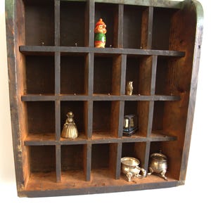 May include: A vintage wooden cubby shelf with multiple compartments, painted dark brown with a green trim. The shelf contains small decorative items, including a gnome figurine, a small owl, a miniature lantern, and two silver-coloured bowls.