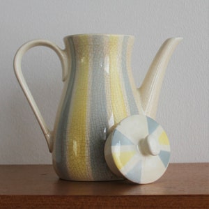 Op de afbeelding: Een keramische theepot met een geel en blauw gestreept ontwerp en een bijpassend deksel. De theepot heeft een gekrakelde glazuur.
