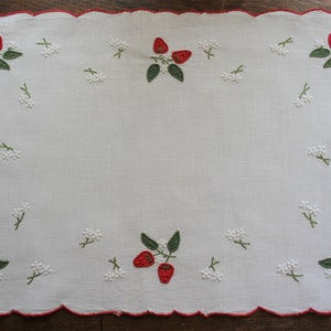 May include: White linen tablecloth with a scalloped edge and embroidered strawberries in red and green.