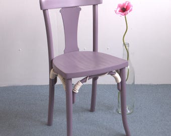 Könnte beinhalten: Ein lilafarbener Holzstuhl mit einem weißen Seil, das in die Beine geflochten ist. Der Stuhl hat ein schlichtes Design mit einer geschwungenen Rückenlehne und einer leicht abgerundeten Sitzfläche.