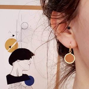 Puede incluir: Un par de pendientes de aro dorados con un colgante de disco marr&oacute;n. Los pendientes cuelgan de la oreja de una persona.