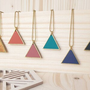 Könnte beinhalten: Sieben dreieckige Anhänger an goldenen Ketten, jeder mit einer anderen Farbe oder einem anderen Muster: weiß, Holzmaserung, Koralle, rosa, blaugrün, marineblau und schwarz.