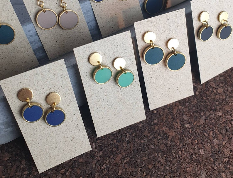 Puede incluir: Surtido de pendientes circulares dorados y de colores expuestos en tarjetas. Los pendientes presentan una variedad de colores, incluyendo azul, verde y marr&oacute;n.