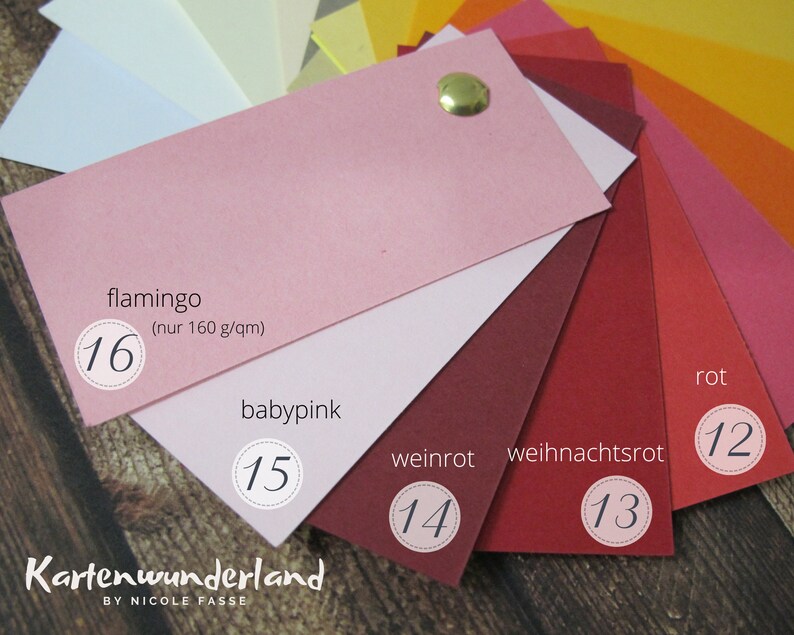 May include: A color chart of paper samples in shades of pink and red. The colors are labeled with German names: flamingo, baby pink, weinrot, weihnachtsrot, and rot. Each color has a number next to it, ranging from 12 to 16.