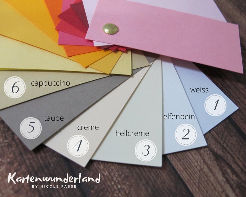 Peut inclure: Un nuancier de 6 teintes diff&eacute;rentes de beige, cr&egrave;me et blanc. Les couleurs sont &eacute;tiquet&eacute;es avec des num&eacute;ros et des noms allemands : 6 cappuccino, 5 taupe, 4 cr&egrave;me, 3 hellcreme, 2 elfenbein, 1 weiss. Le nuancier est &eacute;tiquet&eacute; "Kartenwunderland by Nicole Fasse".