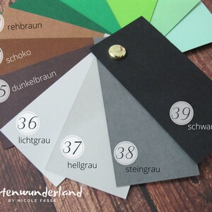 Peut inclure: Un nuancier de 10 teintes diff&eacute;rentes de brun, gris et noir. Les couleurs sont &eacute;tiquet&eacute;es avec des num&eacute;ros et des mots allemands. Le nuancier est en papier et comporte un bouton dor&eacute; au centre.
