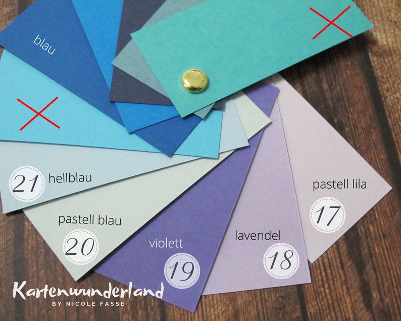 May include: A color chart with 10 different shades of blue, purple, and lavender. The colors are labeled with German words and numbers. The chart is on a wooden surface.