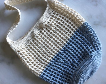 May include: A crocheted tote bag with a white and blue color block design. The bag has a single strap and a mesh pattern.