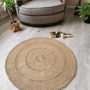 Puede incluir: Una alfombra redonda de ganchillo beige con un dise&ntilde;o en espiral. La alfombra est&aacute; hecha de una fibra natural y tiene una superficie texturizada. La alfombra est&aacute; colocada sobre un suelo de madera gris claro. La alfombra tiene unos 122 cm de di&aacute;metro.