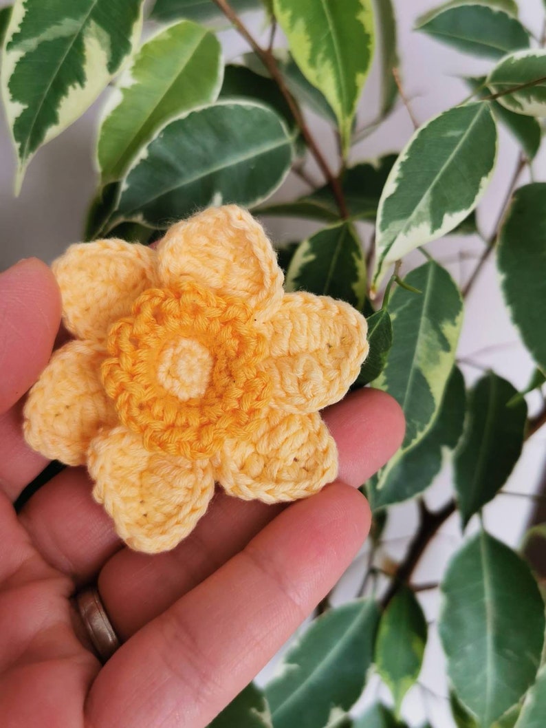 May include: A crocheted yellow flower with a detailed center, held in a hand.