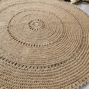 Puede incluir: Una alfombra redonda de yute beige con un dise&ntilde;o en espiral. La alfombra est&aacute; tejida a mano con una superficie texturizada y un borde decorativo. El di&aacute;metro de la alfombra es de aproximadamente 152 cm.