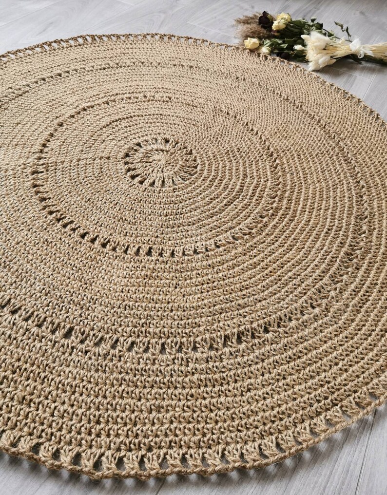 Puede incluir: Una alfombra redonda de yute beige con un dise&ntilde;o en espiral. La alfombra est&aacute; tejida a mano con una superficie texturizada y un borde decorativo. El di&aacute;metro de la alfombra es de aproximadamente 152 cm.