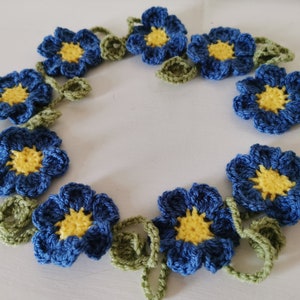 May include: A crocheted garland of blue flowers with yellow centres and green leaves.