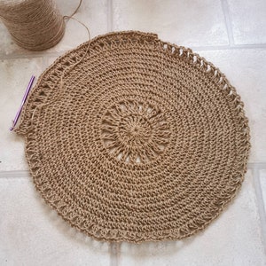 Puede incluir: Proyecto de ganchillo circular inacabado en tonos marr&oacute;n y beige. El centro presenta un dise&ntilde;o de sol. Se ven un ganchillo y un ovillo de hilo.