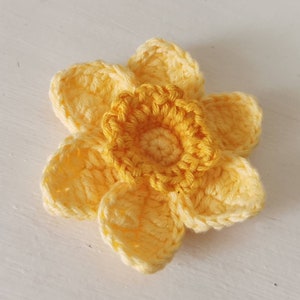 May include: A crocheted yellow daffodil flower with a center made of a darker yellow yarn.