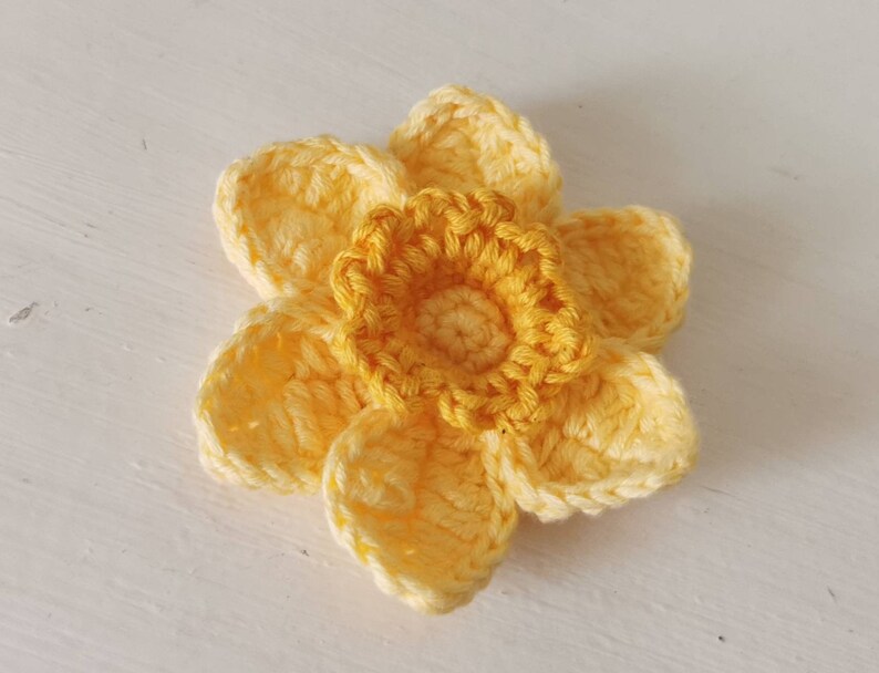 May include: A crocheted yellow daffodil flower with a center made of a darker yellow yarn.