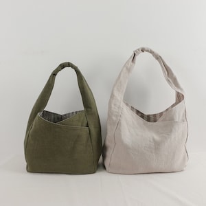 May include: Two hobo-style shoulder bags made of fabric. One bag is olive green with a dark striped interior lining, and the other is beige with a light brown striped interior lining. Both bags feature a single knotted handle and an exterior pocket.