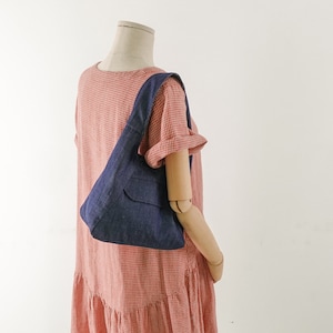 May include: A blue denim tote bag with a small pocket on the front. The bag is being worn by a mannequin wearing a red and white gingham dress.