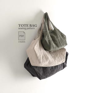 May include: A digital PDF sewing pattern for a tote bag in 3 sizes. The image displays three tote bags hanging vertically, featuring a dark olive green bag on top, a beige bag in the middle, and a dark charcoal grey bag at the bottom.