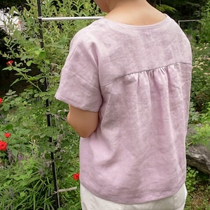 Op de afbeelding: Een lichtpaarse linnen top met een geplooide rug. De top heeft korte mouwen en een ronde hals.