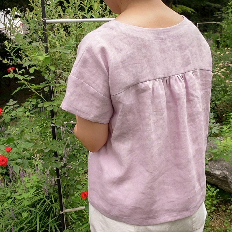 Op de afbeelding: Een lichtpaarse linnen top met een geplooide rug. De top heeft korte mouwen en een ronde hals.