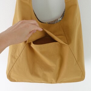 May include: A mustard yellow tote bag with a large pocket on the front. The bag is made of a soft, textured fabric.
