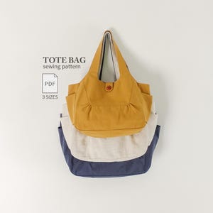 Peut inclure: Un patron de couture numérique pour sac cabas, étiqueté TOTE BAG sewing pattern et PDF 3 SIZES. L'image montre trois sacs cabas empilés en jaune moutarde, blanc cassé et bleu marine, chacun doté de poches latérales et d'un bouton central.