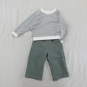 Pode incluir: Uma camisa de manga comprida cinza e branca com uma cal&ccedil;a verde.